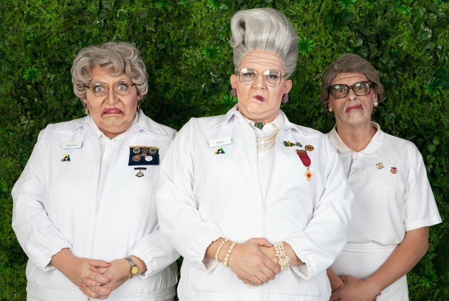Three men dressed as elderly female lawn bowl team wearing white uniforms and wigs.