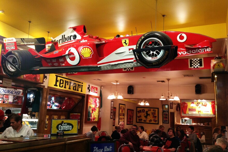 People drinking in a Ferrari-themed bar with a sports car suspended from the ceiling.