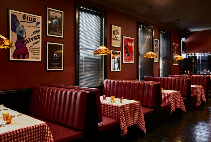 A traditional looking New York diner with checked table clothes and red leather seats.