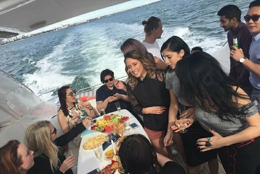Large group of people enjoying a large platter of food and drinks on the boat.
