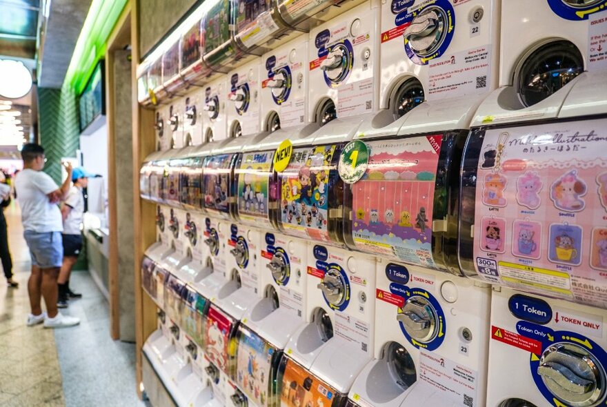 A toy capsule vending wall and in the background people lining up at a food takeaway counter.