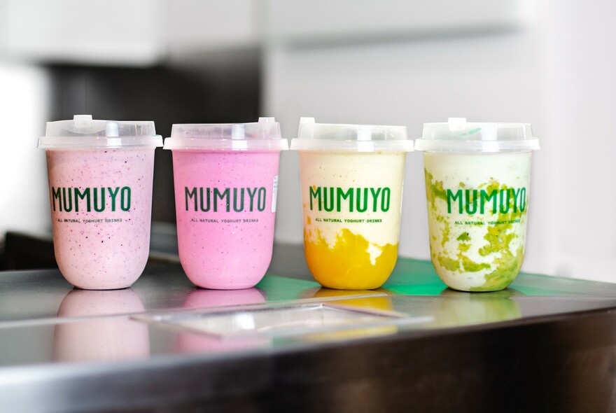 Several flavoured yoghurt drinks in takeaway containers with plastic straws.