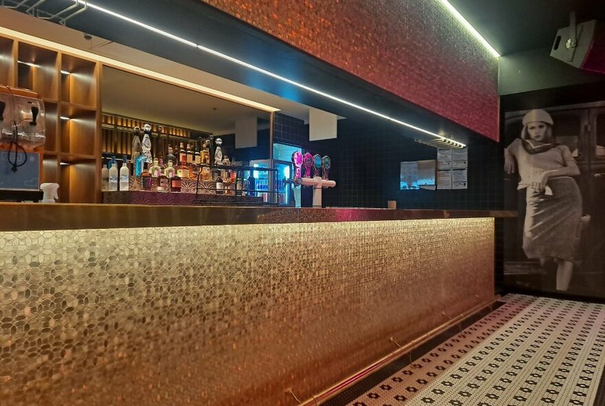 A long gold mosaic bar with tiled floor and drinks.