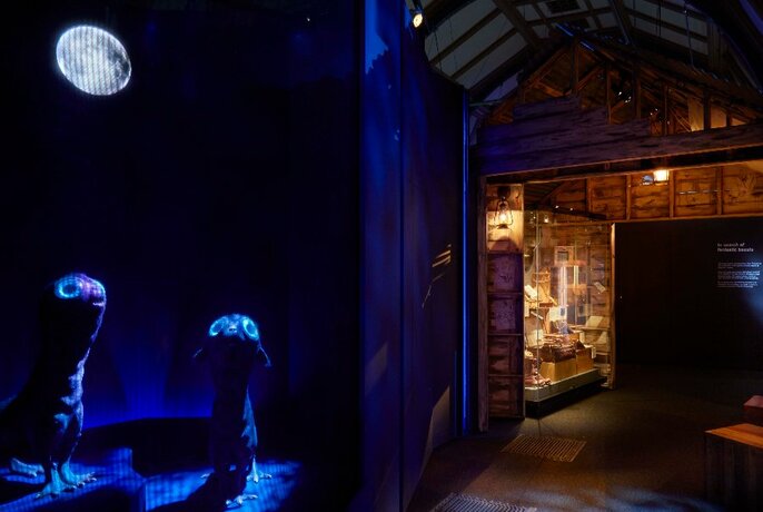 Looking into a museum room, with artefacts on display, two darkly lit strange looking animal creatures in the foreground.