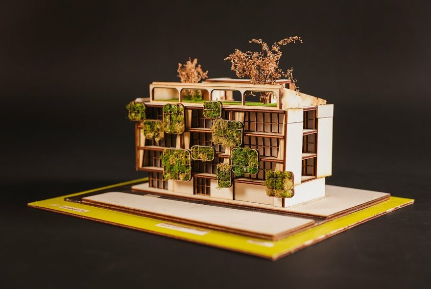 A 3-D model of a multi level building with vertical gardens, made from balsa wood, on a platform.