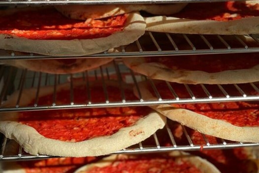 Rows of pizzas on grills in an oven.