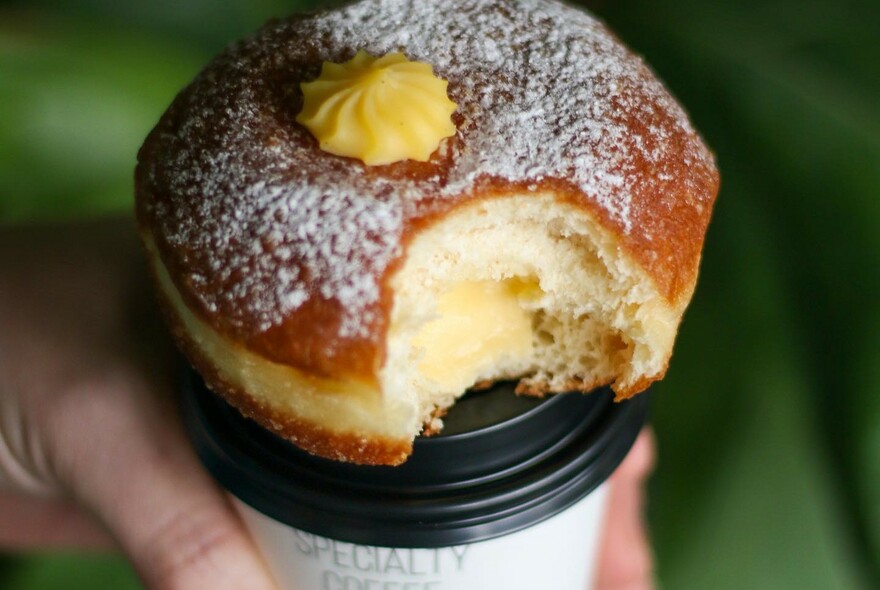 A donut balanced in the top of a takeaway coffee cup.