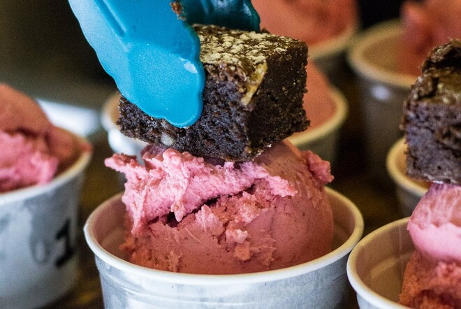 Blue tongs adding a chocolate brownie to cups of pink gelato.
