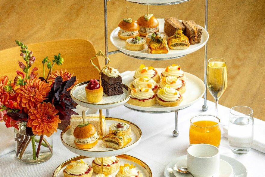 A formal table set for high tea with sweet and savoury treats and orange juice and champagne. 