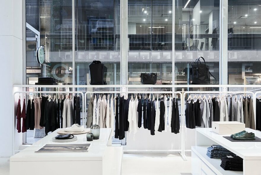 Interior of a sleek and contemporary fashion store, with racks of black and white clothings displayed against floor to ceiling windows looking out onto the street.