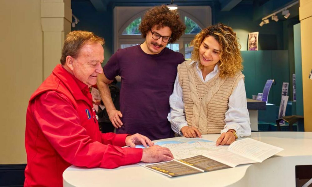 A man in a red jacket showing a woman and a man a map