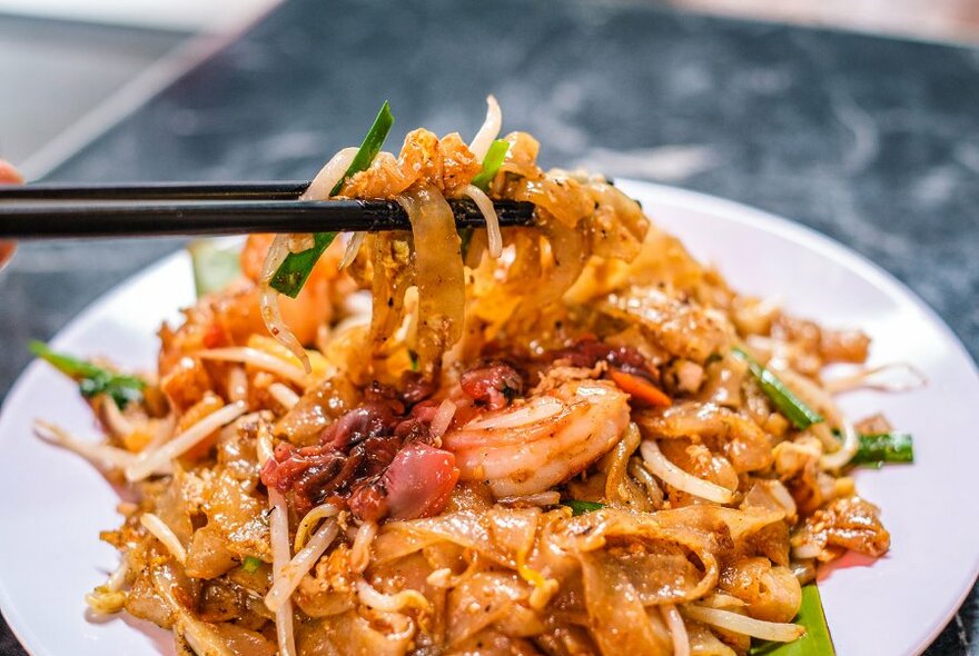 A pair of chopsticks lifting noodles off a restaurant dish. 