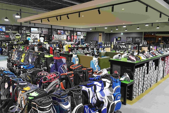 Interior of store selling golfing equipment with many golf bags visible in the foreground and golf shoes on the counter.