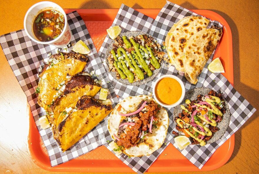 A selection of tacos on check napkins on a orange tray.