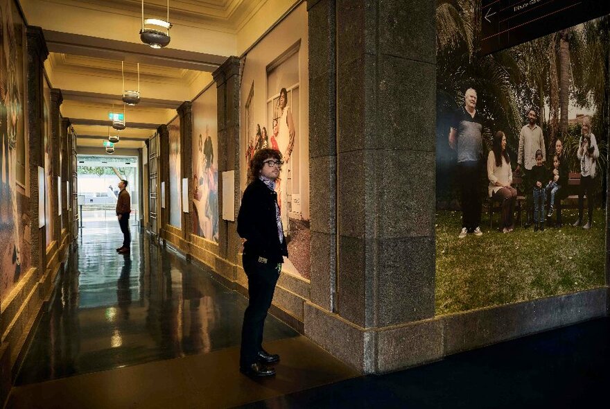 A person at the corner of a corridor with large photographic portraits on the wall.