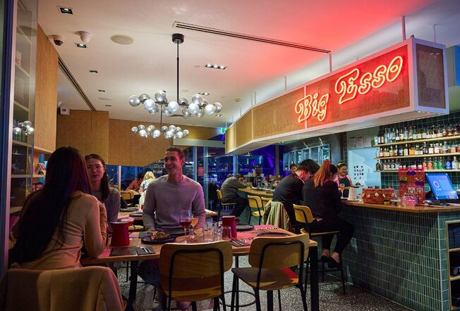 People dining in a casual restaurant with a red neon sign. 