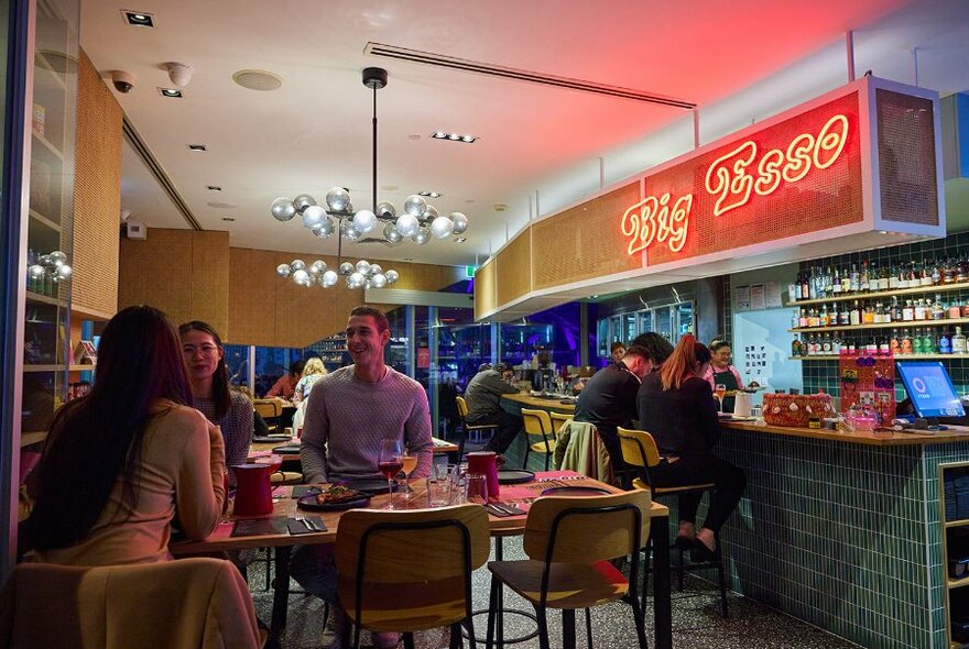 People dining in a casual restaurant with a red neon sign. 