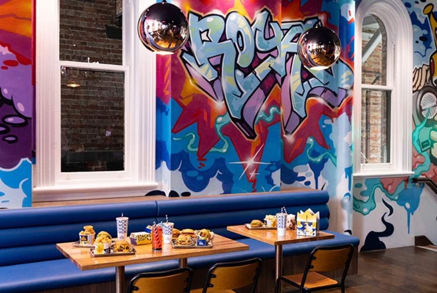 Burger cafe with graffiti decor, blue bench seating and tables with chips and burgers.