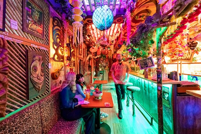 Two girls sharing a cocktail in a colourful tiki bar.