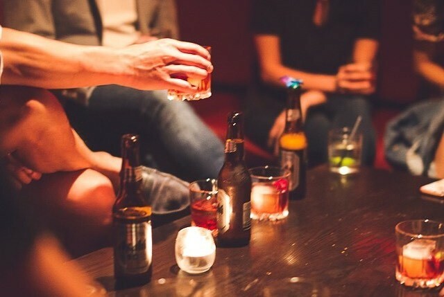 People sitting on couches around a table that holds beer bottles and other drinks in glasses.