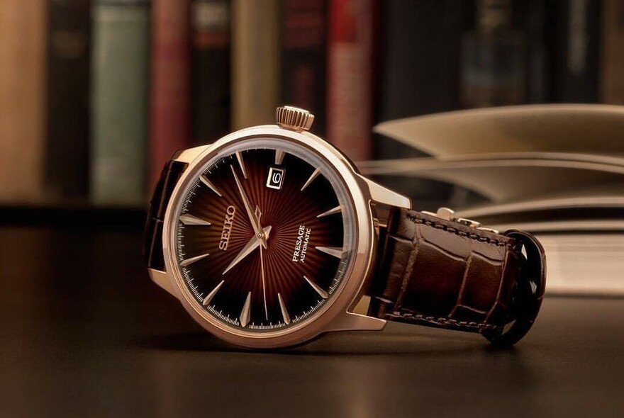 Seiko watch with brown leather watch band, on its side on a table, with bookshelf in background.
