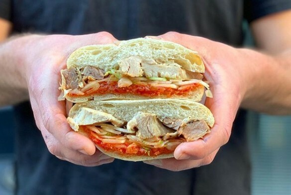 Two hands holding a large meat sandwich with relish.