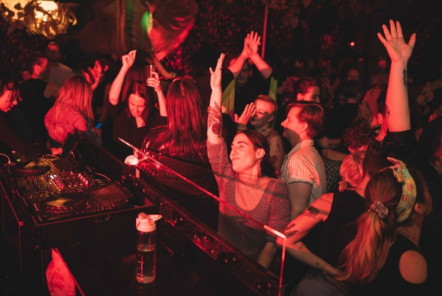 People dancing at a nightclub in front of a DJ's mixing desk.