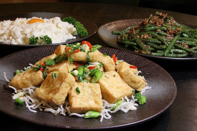 Three dishes, one with fried tofu, one with rice and another with green beans.