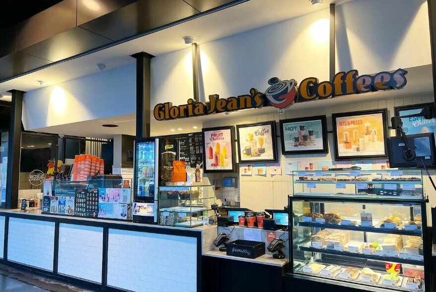 Photo of a takeaway coffee house with white serving bench, refrigerated cabinet with sandwiches and 'Gloria Jean's Coffees' sign above.