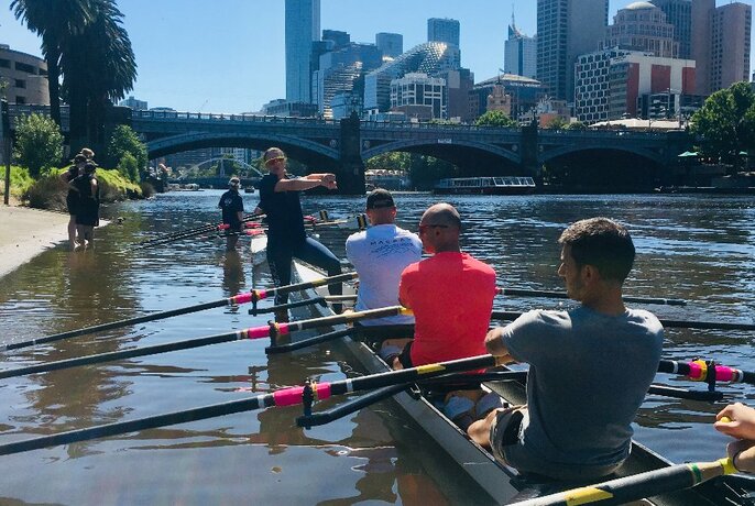 An instructor teaching four men to row on the Yarra River. 