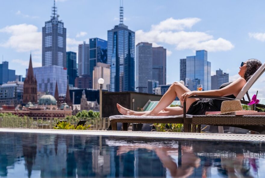 A person lounging in the sun by a pool next to the city skyline.