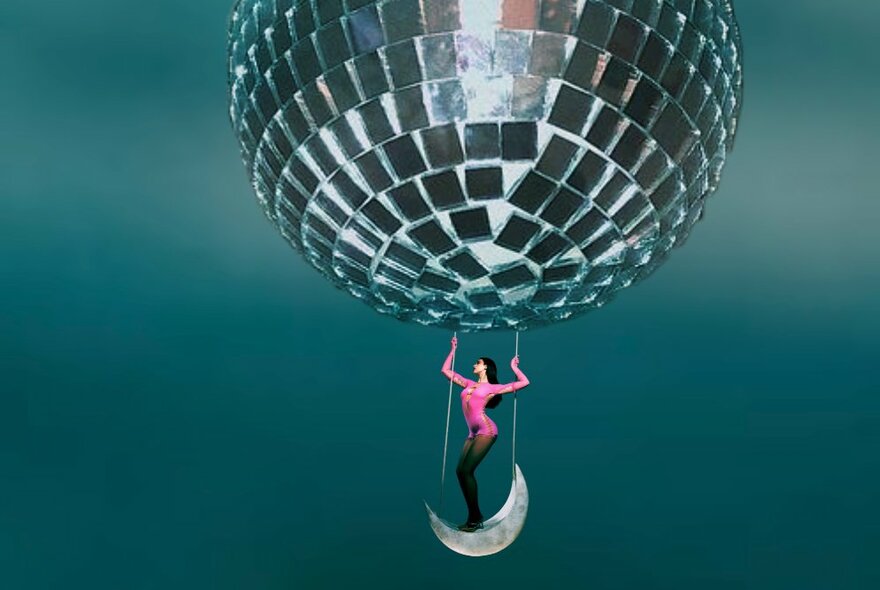 Person in pink balanced on the hanging swing seat of a giant mirror ball.