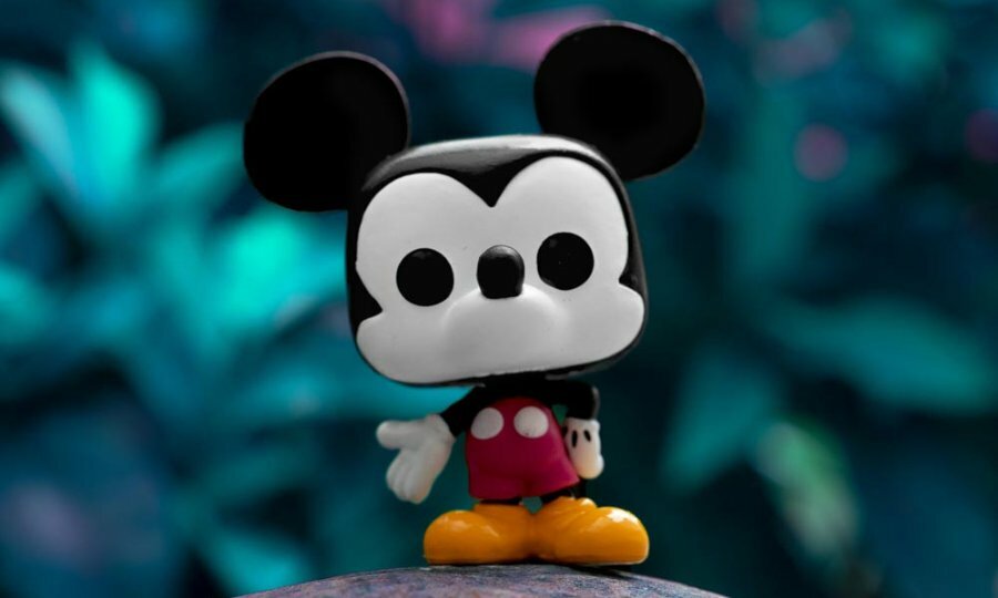 A toy figure of mickey mouse sitting on a rock in front of plants 