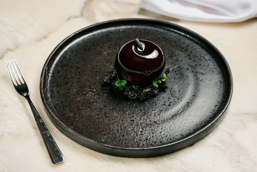 Dark, swirled dessert on dark grey plate, fork to left.