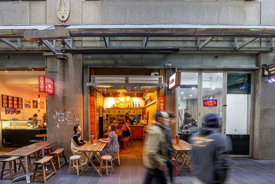 People dining outside a glowing laneway cafe. 