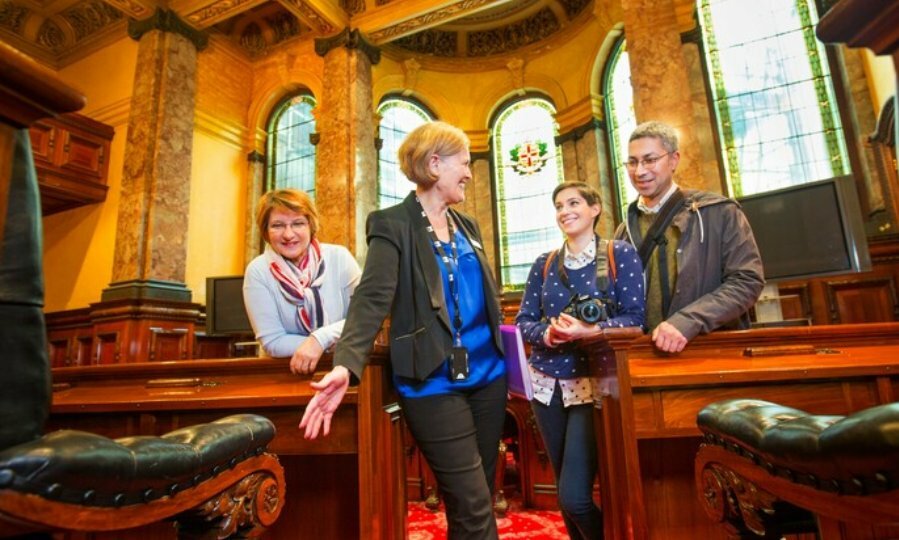 Tour leader showing visitors inside Council Chambers in Melbourne Town Hall