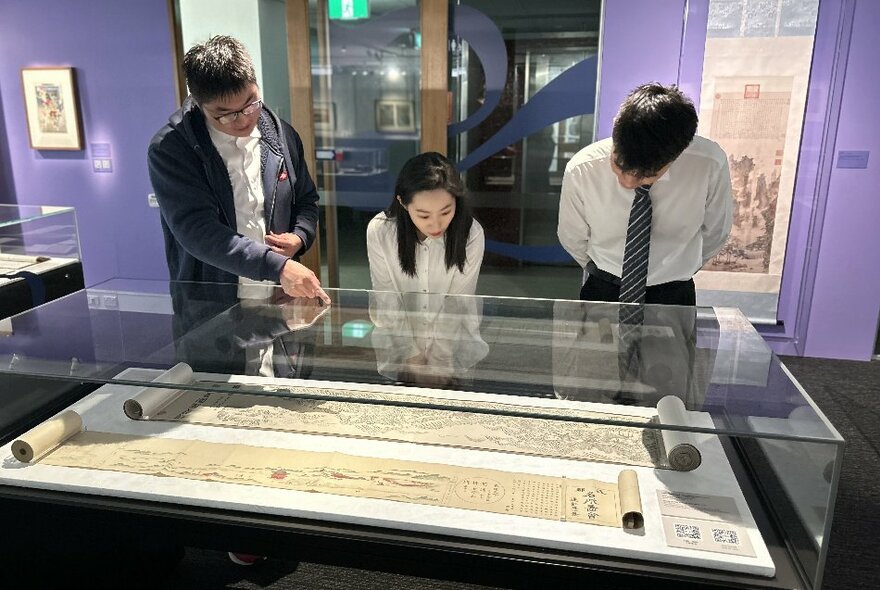 Three people looking at manuscripts on display in a glass case in an exhibition space.