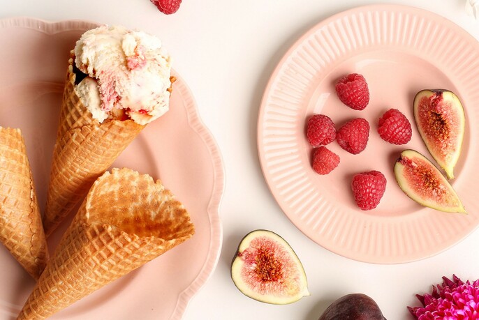 Two pink plates, one with cones and ice cream and the other with strawberries and figs.