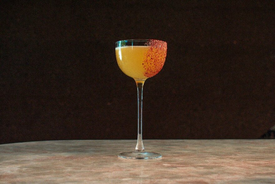 A cocktail in a long-stemmed glass trimmed with orange zest, on a counter.