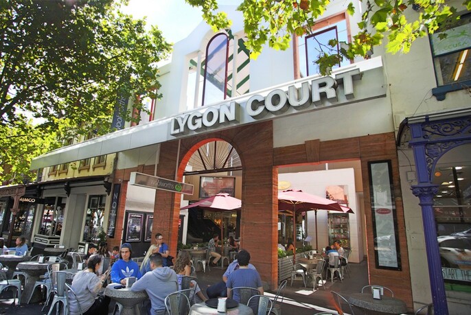 People seated at small tables outside Lygon Court Shopping Centre.
