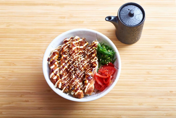 A rice and meat bowl with condiments and a pot of tea. 