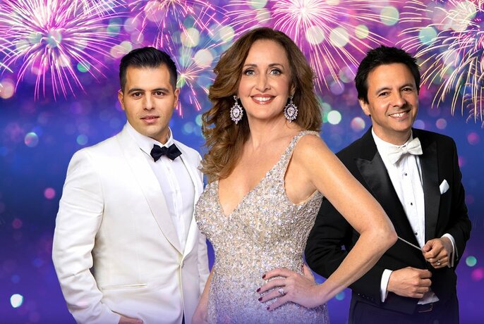 Three performers in formal evening wear stand against a backdrop of fireworks.