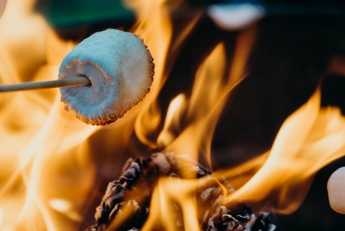 Marshmallow on a long skewer being toasted over an open flame.