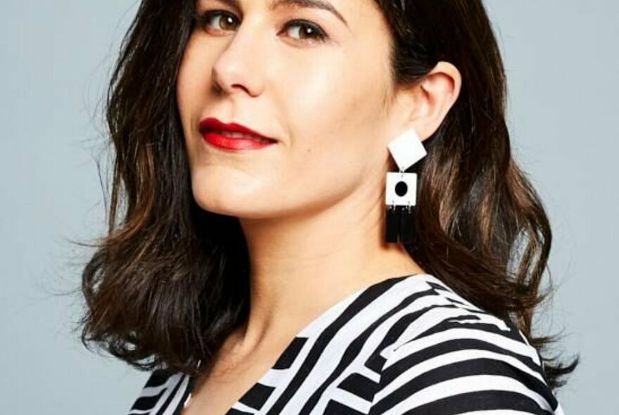 Journalist and TV presenter Jan Fran, her head turned to look at camera, her brown hair at shoulder length, smiling slightly and wearing a geometric hanging white earring.