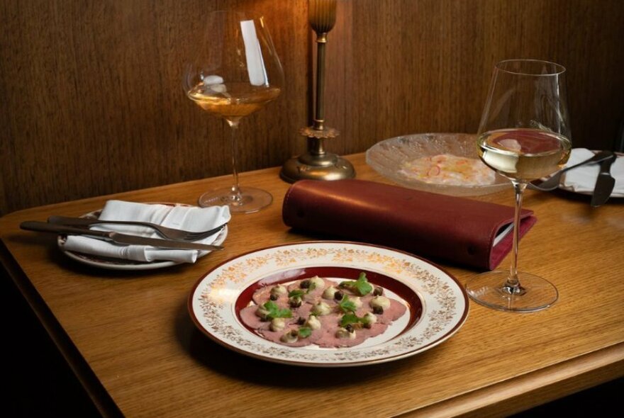 Wooden table with cold meat dish and two white wine glasses