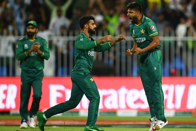 Three members of Pakistan's T20 men's cricket team wearing their distinctive dark green uniforms, celebrating on the cricket field, spectators in the background.
