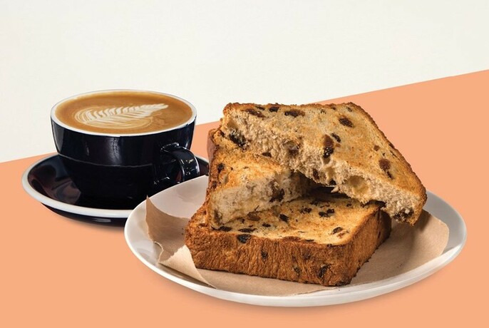 Cup of coffee in black cup and saucer next to a plate of toasted raisin bread.
