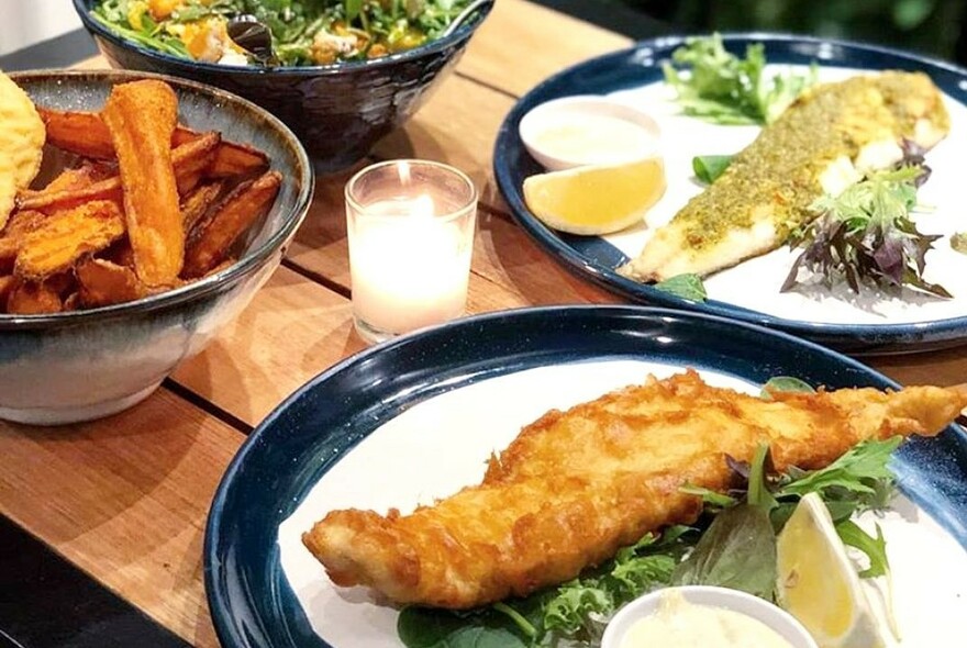 Grilled and fried fish and chips on plates, with a bowl of chips and a bowl of salad.