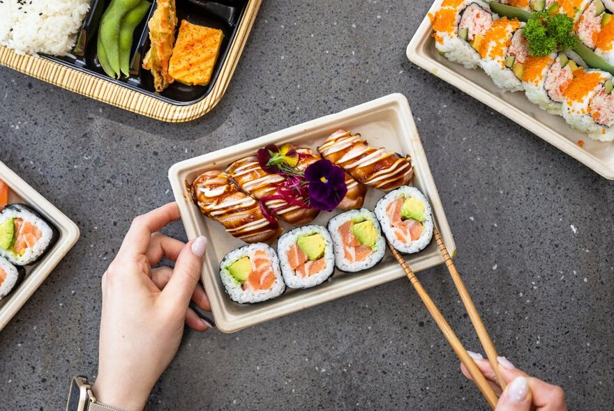 Hands holding a sushi tray and chopsticks.