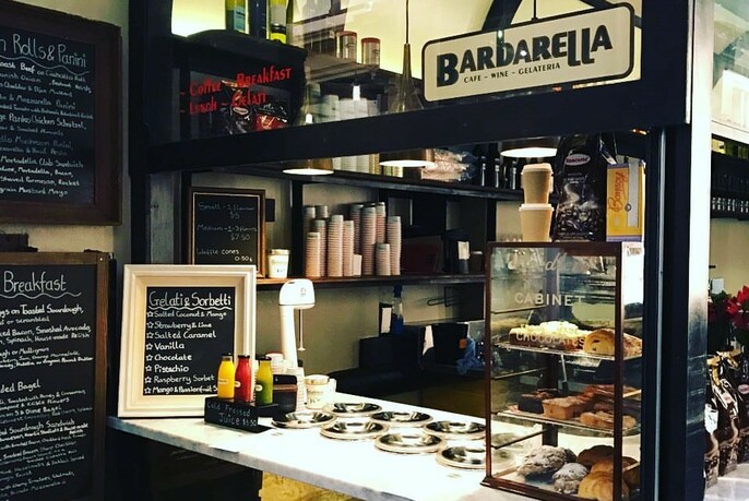 Barbarella counter with blackboard menus, signs and glass display filled with cakes, kitchen in the background.